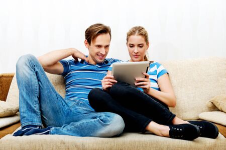 Young couple sitting at home and looking for something on tablet.の写真素材