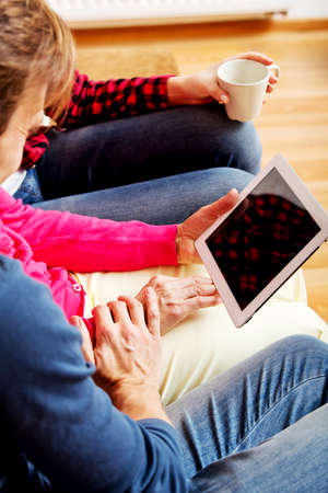 Young couple with old woman sitting on couch and watching something on tablet.の写真素材