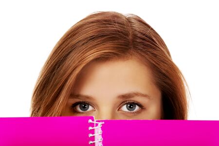 Teenage woman hiding her face behind a notebook.の写真素材