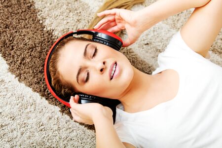 Young woman lying on the carpet and listenig a music in headphones.の写真素材