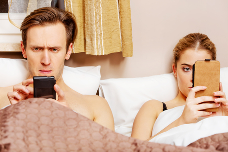 Young couple in a bed with mobile phones.の写真素材