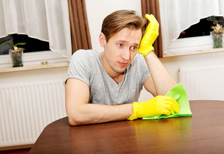 Tired man sitting behind the desk with cloth and gloves.