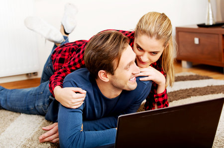 Happy couple lying on the floor with laptop.