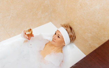 Senior woman relaxing in bath with glass of champagne.の写真素材
