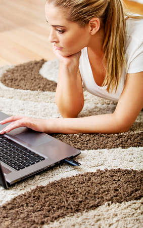 Focused young woman using laptop while lying on floor.の写真素材