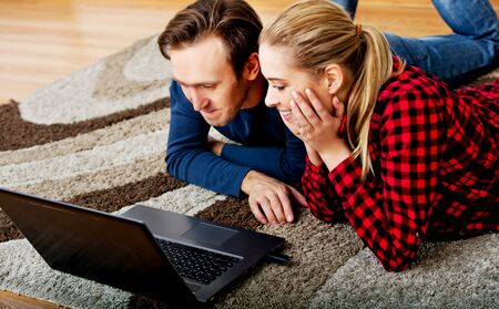 Happy couple lying on the floor with laptop.の写真素材