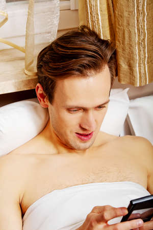 Young man lying on bed and using mobile phone.の写真素材