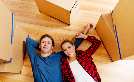 Happy couple lying on the floor in new home with cordboard boxes around.