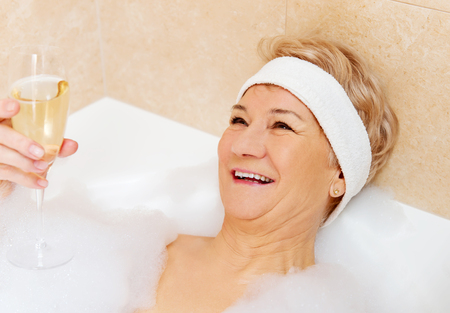 Senior woman relaxing in bath with glass of champagne.の写真素材