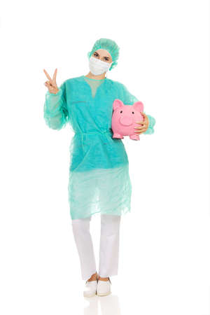 Female surgeon doctor with piggy bank shows victory sign.の写真素材
