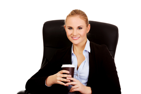 Smiling business woman sitting on a chair and holding cup of coffee.の写真素材