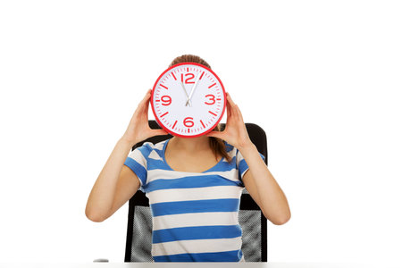 Teenage woman covering her face with a clock.
