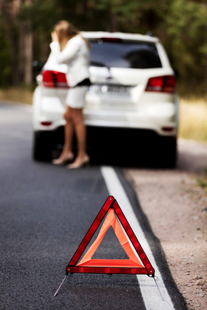 Red warning triangle and broken car on the road in the middle of forrest.の写真素材