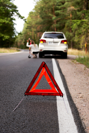 Red warning triangle and broken car on the road in the middle of forrest.の写真素材