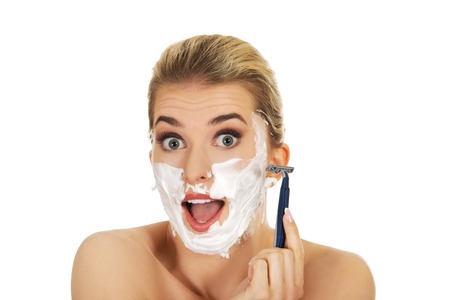 Young shocked woman shaving her face with a razor, isolated on whiteの写真素材