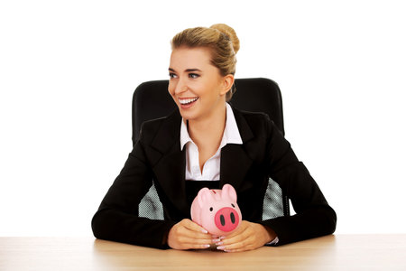 Businesswoman with a piggybank behind the desk.の写真素材