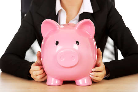 Worried businesswoman with a piggybank behind the deskの写真素材