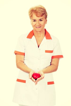 Smile elderly doctor or nurse holding red toy heart.の写真素材