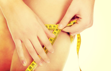 Young woman measuring her thigh.