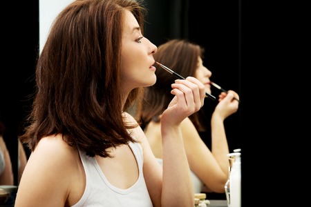 Woman applying lipstick in bathroom.の写真素材