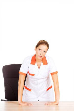 Tired young female doctoror nurse standing behind the desk.の写真素材