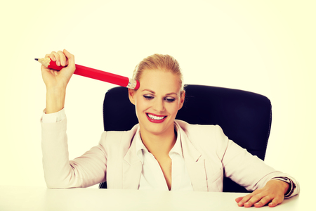 Smiling business woman sitting behind the desk and holding huge pen.の写真素材