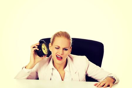 Business woman sitting behind the desk and listen to alarm clock.の写真素材