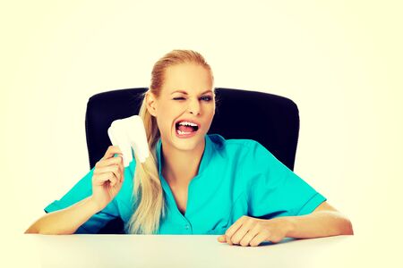 Funny female dentist sitting behing the desk and holding oversized tooth model.の写真素材