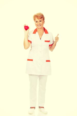 Smile elderly female doctor or nurse holding red toy heart.の写真素材