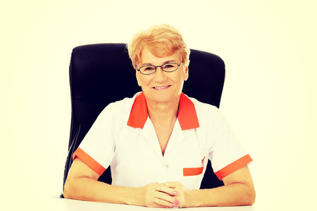 Smile elderly female doctor or nurse in glasses sitting behind the desk.の写真素材