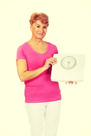 Smiling old woman holding weight scale.の写真素材