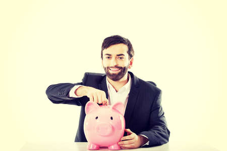 Young successful businessman putting a coin to piggybank.の写真素材