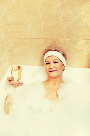 Senior woman relaxing in bath with glass of champagne.の写真素材
