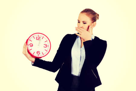 Yawning business woman holding office clock.の写真素材