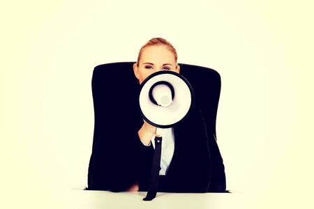 Business woman sitting behind the desk and screaming through a megaphone.の写真素材