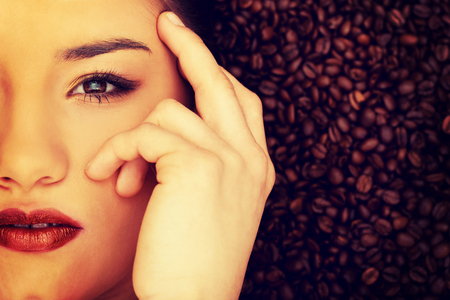Attractive woman lying in coffee grains touching face.の写真素材