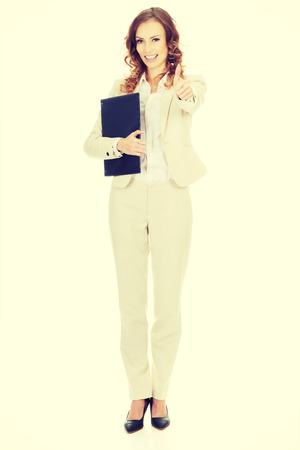 Smiling businesswoman showing thumbs up with clipboard.の写真素材