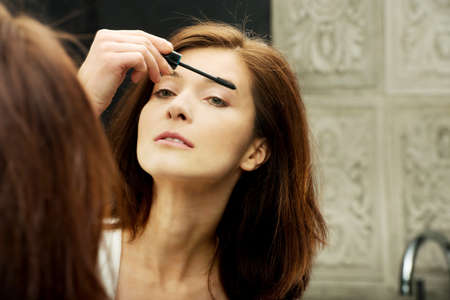Woman using mascara in bathroom mirror.の写真素材