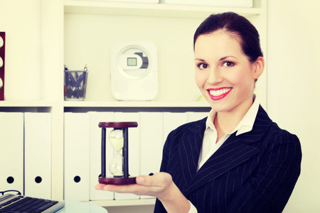 Business woman holding hourglass. Sitting in an office.