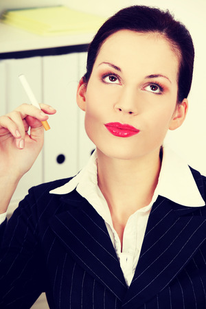 Beautiful business woman is holding cigarette, in office.の写真素材
