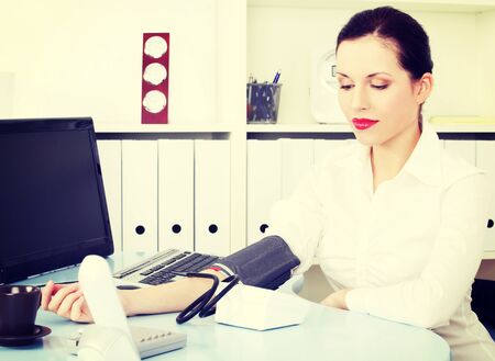 Beautiful business woman is measuring her blood pressure in office.の写真素材