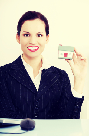 Business woman is holding a miniature house, in office. Selling house concept.の写真素材
