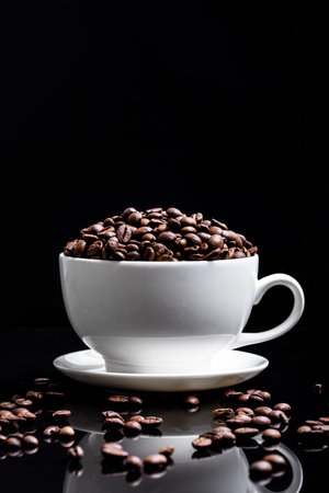 White cup with coffee seeds on black background.
