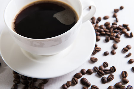 White cup with coffee and coffee seed on the table.