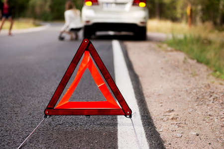 Red warning triangle and broken car on the road in the middle of forrest.の写真素材