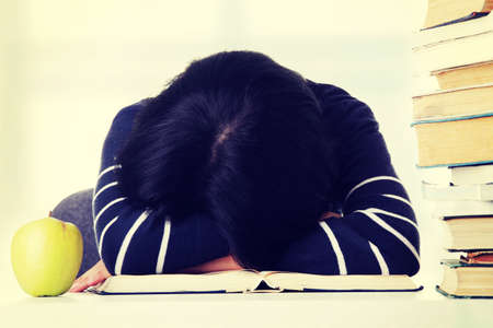 Young woman sleeping on desk next to pile of books, isolated on whiteの写真素材