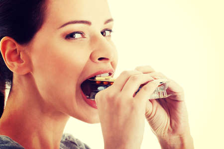 Casual beautiful woman trying to eat blister of pills. Isolated on white.の写真素材