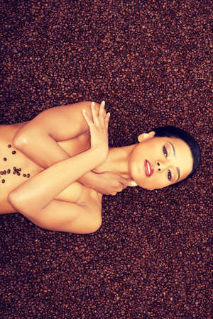 Attractive naked woman lying in coffee grains. Up front view.の写真素材