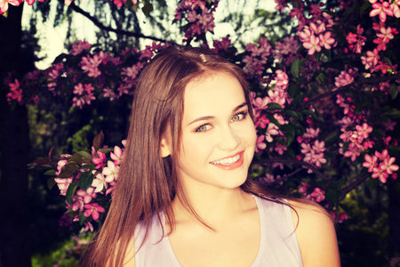 Attractive young woman outdoor view. There are blossom flowers behind her.