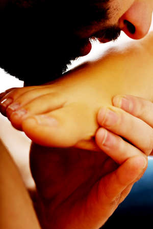 Hndsome man kissing woman's foot with desireの写真素材